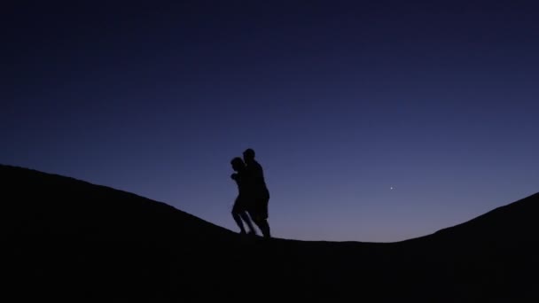 Ζευγάρι silhouetted εναντίον τον νυχτερινό ουρανό στο λόφο — Αρχείο Βίντεο