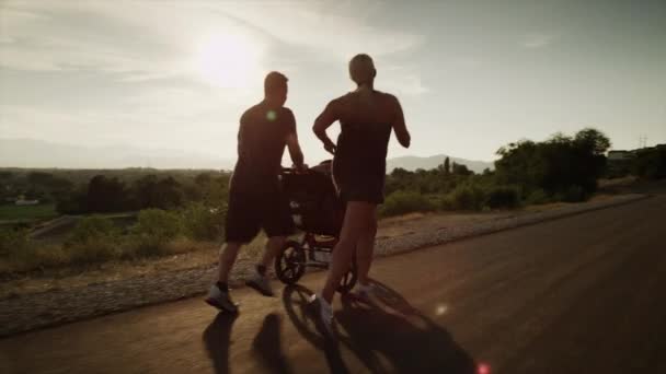 Couple avec voiture de bébé courant sur la route ensoleillée — Video