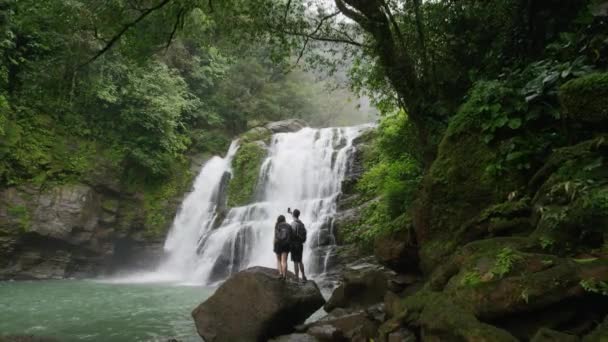 Couple admiring waterfall in rain forest — Stock Video