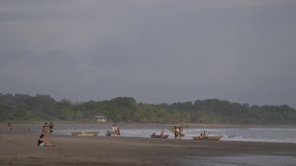 Gente en la playa con tablas de surf y barcos — Vídeos de Stock