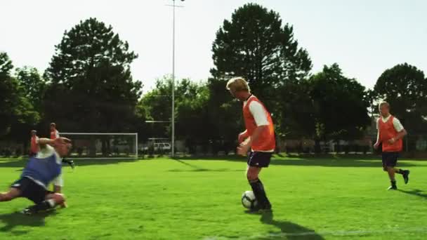 Игроки дриблинг мяч по футбольному полю — стоковое видео