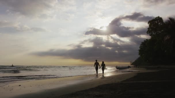 日没時にビーチを歩くカップル — ストック動画
