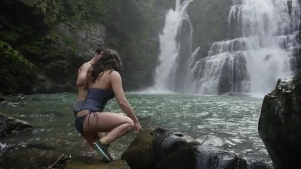 Pareja entrando agujero de natación cerca de cascada — Vídeo de stock