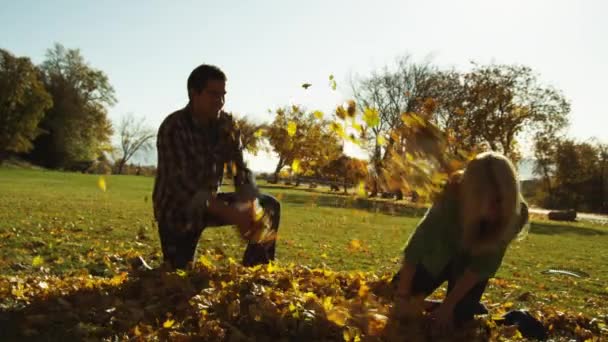 Άντρας και η νεαρή γυναίκα που ρίχνουν τα φύλλα στο πάρκο — Αρχείο Βίντεο
