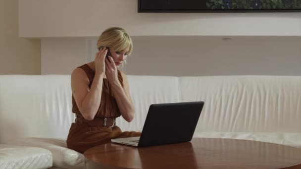 Dizüstü bilgisayar kullanan ve cep telefonuyla konuşan kadın. — Stok video