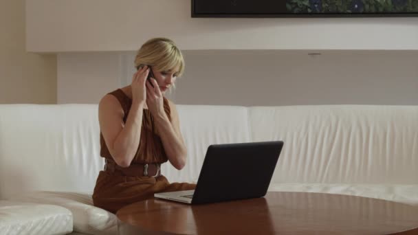 Woman using laptop and talking on mobile phone — Stock Video