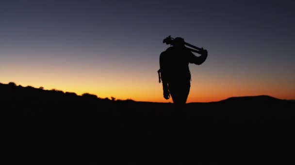 Sylwetka fotograf chodzenie w pustyni na zachodzie słońca — Wideo stockowe