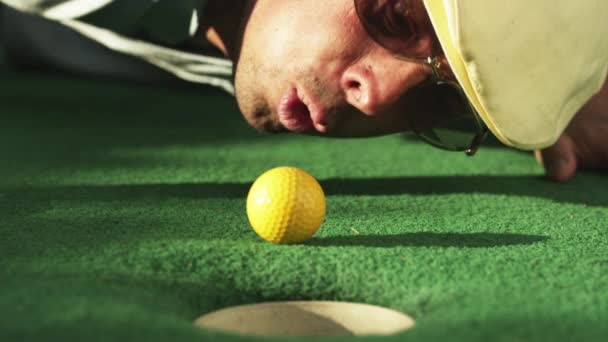 Hombre soplando pelota de golf hacia el agujero — Vídeo de stock