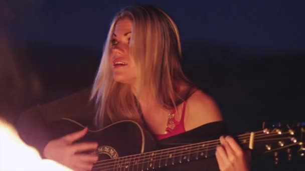 Женщина играет на гитаре и поет у костра — стоковое видео