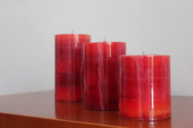 Farklı boyutlarda üç kırmızı mum, kiraz rengi taban ve beyaz arkaplan..