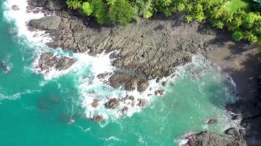 Okyanus dalgasının beyaz sprey ve köpükle kayalık kayalıklara çarptığı hava görüntüsü fırtınadan sonra derin mavi deniz suyuna