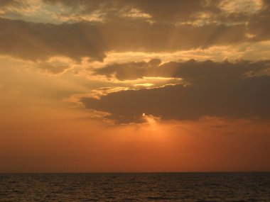 Sakin bir denizin üzerinde batan güneş ışınları