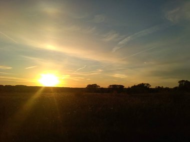 Güneşin günbatımı ışınları bulutlardan yansıyor ve bir Eylül akşamı tarlayı aydınlatıyor.