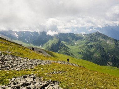 Sırt çantalı bir yürüyüşçü dağların arka planındaki çimenli yamaca gider. Arkadan bak. Arkhyz 'de güzel güneşli bir gün. Sağlıklı yaşam tarzı, yürüyüş aktivitesi, yürüyüş macerası kavramı