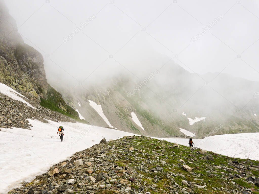 Group of tourists with backpacks rises to the top along a snowy slope in the fog. The concept of a healthy lifestyle, trekking, hiking adventures.
