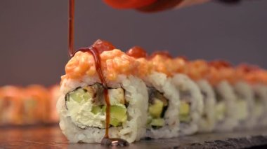  Mutfakta bol bol yemek pişir ve iştah açıcı bir şekilde suşiyi unagi sosuyla doldur, sosun damlaları tabaklara damlasın. Asya mutfağı, somon, yılan balığı, salatalık ve avokado. Siyah arka planda siyah taş plaka