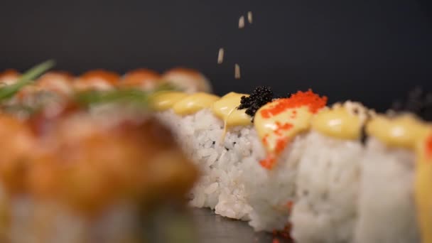 手袋のシェフが お客様に出す前にゴマを使ったお寿司セットを食欲をそそりきれいに飾ります 鮭とトビコのキャビアとウナギとアボカド 暗い背景の黒い石板 — ストック動画