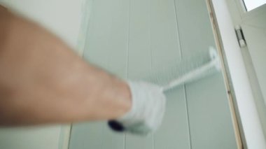 Bir adam silindirle duvar boyuyor. Odada tamirat yapan bir adam. Modern iç mekan. Tavan arasının güzel tasarımı. Kendini soyutlama. Karantinaya alın. Yüksek kaliteli onarım. Kapat.