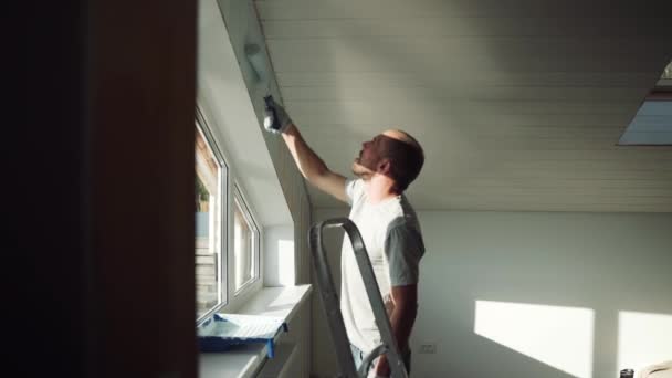 Muž namaluje stěnu kolečkem. Muž dělá opravy v místnosti. Moderní interiér v domě. Krásný design podkrovní podlahy. Sebeizolace. Karanténa. Kvalitní opravy — Stock video
