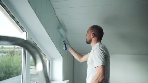 Muž namaluje stěnu kolečkem. Muž dělá opravy v místnosti. Moderní interiér v domě. Krásný design podkrovní podlahy. Sebeizolace. Karanténa. Kvalitní opravy — Stock video