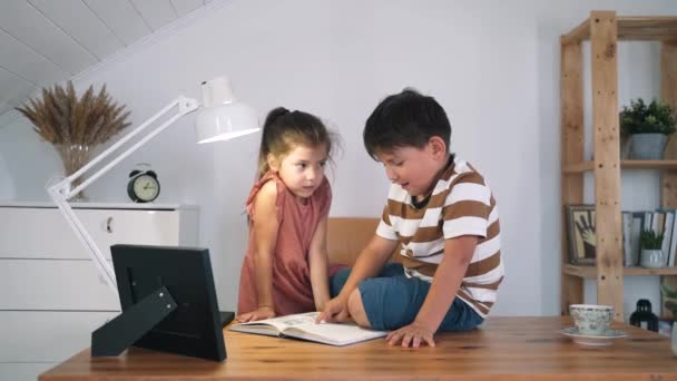 Bir erkek ve bir kız masada oturan bir kitap okuyorlar. Çocuklar ev ödevlerini yapıyorlar. Evde eğitim. Kendini soyutlama. Çocuk dersleri var. Yavaş çekim — Stok video