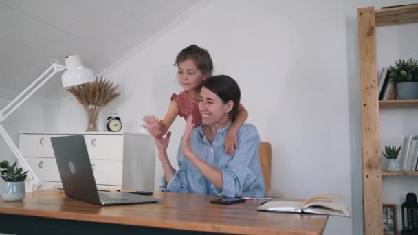 Жінка і дитина спілкуються онлайн. Жінка і дівчина посміхаються і махають руками перед ноутбуком. Дівчина обіймає матір. Близькі стосунки в родині. Фріланс. Самоізоляція — стокове відео