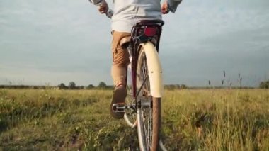 Bir adam retro bisiklet sürüyor. Adam pedal çeviriyor. Bir bisikletçi sahaya çıkar. Bir gezgin. Modaya uygun bir bisiklet. Kendini soyutlama. Açık hava eğlencesi. Köy hayatı. Yavaş çekim