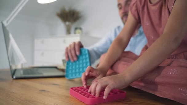 En man och ett barn leker Poppit. En man som jobbar på en bärbar dator tar en paus och leker Poppit med en tjej. En anti-stress leksak. Populära trender 2021. Självisolering. Slappna av — Stockvideo