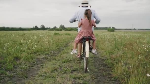 En man bär ett barn på en retrocykel. En man och en flicka kör genom ett blomfält. Retrostil. En modern cykel. Självisolering. Familjesemester. Livet på landet. Långsamma rörelser — Stockvideo