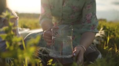 Bir kadın elinde bir sürahi ile içki tutuyor. Sürahideki içecek güneşte parlıyor. Aile doğada dinleniyor. Yeşil çayır. Kendini soyutlama. Yavaş çekim