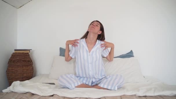 Kvinnan sträcker på sig sittande i sängen. Yoga. Vacker pyjamas på en kvinna. Mysig säng. God morgon. Morgonövning. En hälsosam livsstil. Långsamma rörelser — Stockvideo