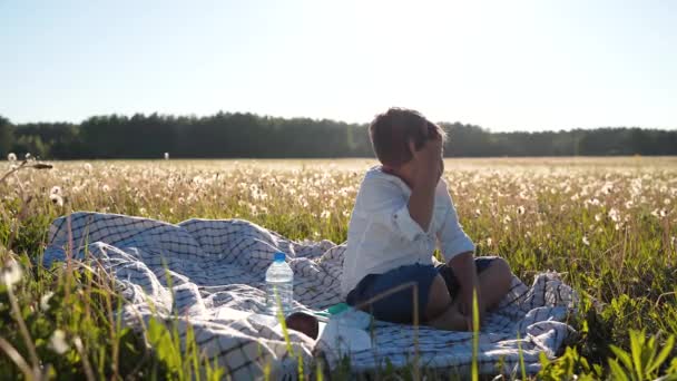 En drömsk pojke. Barnet reflekterar. En pojke sitter på ett fält. Tankar om det viktigaste. Livets filosofi. Friluftsliv. En extraordinär värld. Planeten är i fara. En hälsosam livsstil — Stockvideo