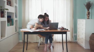 Annem evde çalışıyor. Masada oturan küçük bir çocuk. Anne ve oğlu birlikte iyi vakit geçiriyorlar. Birlikte oynuyorlar. Uzaktan kumanda. Aile bireysel izolasyonda. Merkez ofis. Karantinaya alın. Salgın hastalık. Kriz.