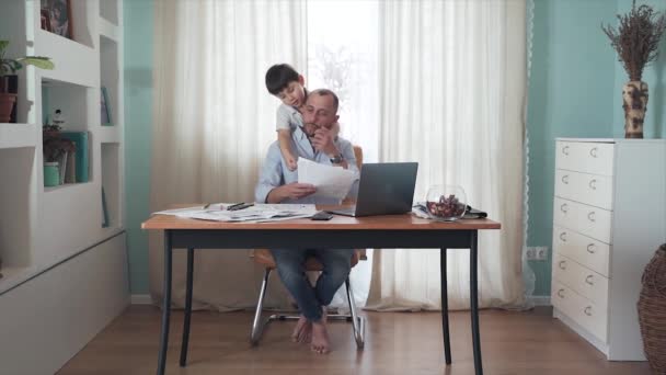 Parent working from home. SLOW MOTION Remote work. Family on self-isolation. Home office. A man is working at a table. The son interferes with the fathers work. Dad gets annoyed. Quarantine. Epidemic — Stock Video