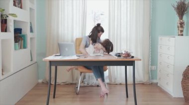 Evde, masada internetten çalışan bir kadın. Anne kızını kucaklıyor. Annem biraz ara verdi. Uzaktan kumanda. Aile bireysel izolasyonda. Merkez ofis. Mutlu bir çocukluk. Karantinaya alın. Salgın.