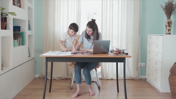 Mère travaillant en ligne de la maison à la table. Un petit garçon est assis sur la table à dessiner. Le garçon est heureux avec sa mère. Famille isolée. Bureau à domicile. Heureuse enfance quarantaine Épidémie — Video