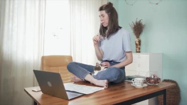 İnternette masada oturan bir kadın. Kız bir şey düşünüyor ve kedisini okşuyor. Hayvanların korunması. Uzaktan kumanda. Merkez ofis. Kendini soyutlama. Karantinaya alın. Salgın.