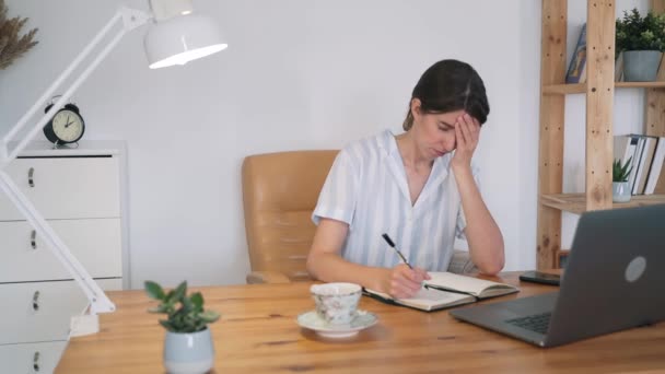 Una donna lavora in un portatile. Una giovane donna in pigiama è stanca e si strofina i templi. Freelance. Auto-isolamento. Sovraccarico. Donna d'affari. Lavora a casa. Consultazione online — Video Stock