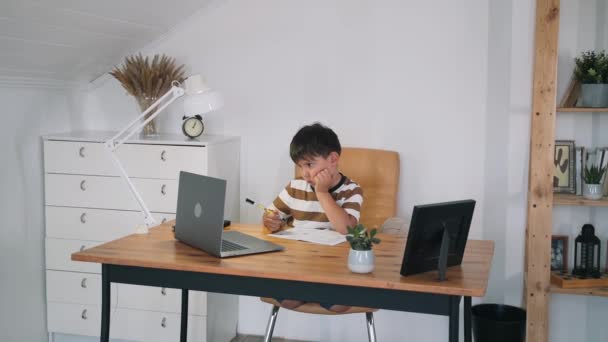 Un niño realiza una tarea en una lección en línea. El niño se comunica en línea mientras está sentado en la mesa. El niño aprende en la computadora. Educación en el hogar. Entrenamiento en línea Autoaislamiento Cámara lenta — Vídeo de stock