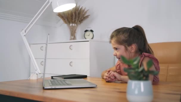 Dziewczyna patrzy na laptopa. Dziecko komunikuje się online siedząc przy stole. Dziecko uczy się w sieci. Edukacja domowa. Światło lampy stołowej. Trening online Samoizolacja Spowolniony ruch — Wideo stockowe