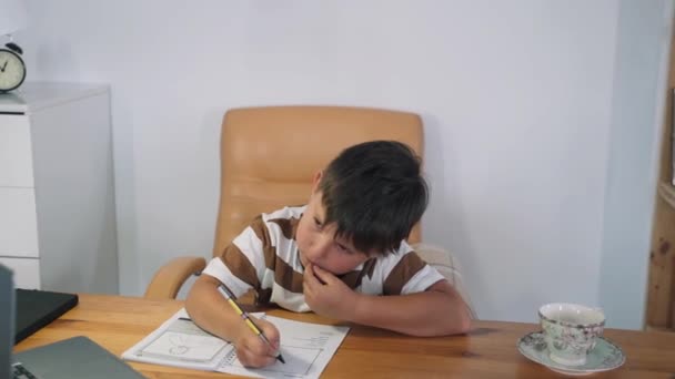Um menino executa uma tarefa em uma lição online. A criança se comunica online enquanto está sentada à mesa. A criança aprende no computador. Educação doméstica. Treinamento online Auto-isolamento Movimento lento — Vídeo de Stock