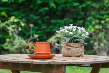 Fincan kahve ve çiçeklerle ağaç arka planda.