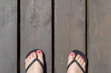 Yuvarlak, ahşap iskele manzaralı, parmak arası terlik giymiş kadınların ayakları..