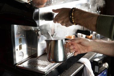 Yakın plan kadın elleri kafede profesyonel metal makine kullanarak kahve yapıyor. Barista sütü ısıtıyor köpüğü köpükle çırpıyor..