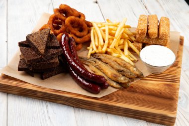 Bira aperatifleri. Kızarmış sosis, patates kızartması, kızarmış ekmek, soğan halkaları, peynir çubukları. Masanın üzerinde.