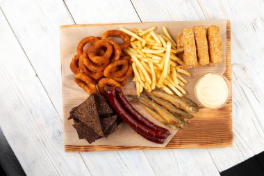Bira aperatifleri. Kızarmış sosis, patates kızartması, kızarmış ekmek, soğan halkaları, peynir çubukları. Masanın üzerinde.