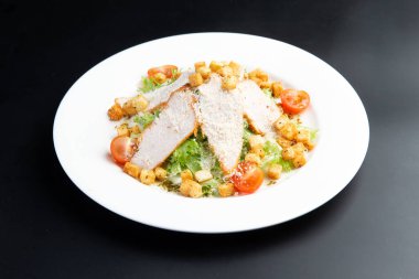 Tavuklu salata ve kızarmış ekmek. Sezar salatası. Karanlık bir arka planda bir tabakta