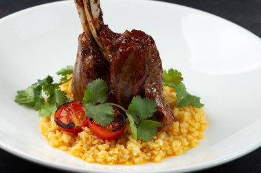 Risotto yastığında kuzu şişi, siyah bir arka planda bir tabakta.