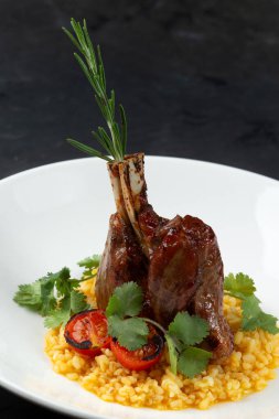 Risotto yastığında kuzu şişi, siyah bir arka planda bir tabakta.