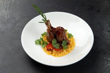 Risotto yastığında kuzu şişi, siyah bir arka planda bir tabakta.